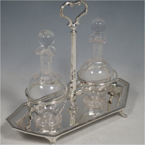 A Sterling Silver oil and vinegar set, having an octagonal boat-shaped body with applied reed-edged borders, a two-bottle frame with loop handle, a pair of hand-cut round crystal bottles with stoppers, and all sitting on four cast scroll feet. Made by Goldsmiths & Silversmiths of London in 1929. The dimensions of this fine hand-made silver oil and vinegar set are length 23 cms (9 inches), height 20 cms (8 inches), width 10 cms (4 inches), and the base weighs approx. 495g (16 troy ounces).   