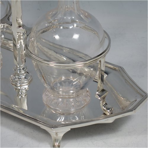 A Sterling Silver oil and vinegar set, having an octagonal boat-shaped body with applied reed-edged borders, a two-bottle frame with loop handle, a pair of hand-cut round crystal bottles with stoppers, and all sitting on four cast scroll feet. Made by Goldsmiths & Silversmiths of London in 1929. The dimensions of this fine hand-made silver oil and vinegar set are length 23 cms (9 inches), height 20 cms (8 inches), width 10 cms (4 inches), and the base weighs approx. 495g (16 troy ounces).   