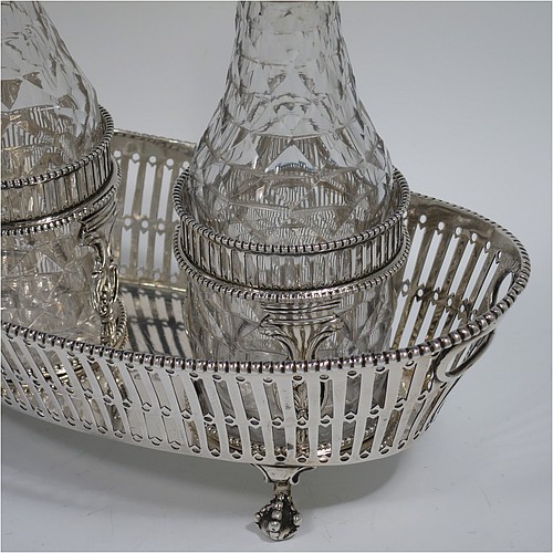 An Antique Georgian Sterling Silver oil and vinegar set, having an oval boat-shaped body with hand-pierced decoration and applied bead-edged borders, with cut-out loop side handles, a pair of hand-cut crystal bottles with stoppers in matching round galleried frames, and all sitting on four cast claw and ball feet. Made by Thomas Northcote of London in 1792. The dimensions of this fine hand-made antique silver oil and vinegar set are length 21.5 cms (8.5 inches), height (excl. bottles) 9 cms (3.5 inches), width 11.5 cms (4.5 inches), and with a total weight of approx. 400g (12.9 troy ounces). Please note that this item is crested. 