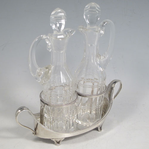 Antique Georgian sterling silver oil and vinegar set, having an oval boat-shaped body with applied bead-edged borders, two loop side handles, a pair of hand-cut crystal bottles with stoppers, and all sitting on four flange feet. Made by John Schofield of London in 1782. The dimensions of this fine hand-made silver oil and vinegar set are length 16.5 cms (6.5 inches), height (excl. bottles) 6.5 cms (2.5 inches), width 6.5 cms (2.5 inches), and the base weighs approx. 152g (5 troy ounces).