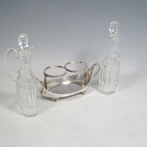 Antique Georgian sterling silver oil and vinegar set, having an oval boat-shaped body with applied bead-edged borders, two loop side handles, a pair of hand-cut crystal bottles with stoppers, and all sitting on four flange feet. Made by John Schofield of London in 1782. The dimensions of this fine hand-made silver oil and vinegar set are length 16.5 cms (6.5 inches), height (excl. bottles) 6.5 cms (2.5 inches), width 6.5 cms (2.5 inches), and the base weighs approx. 152g (5 troy ounces).