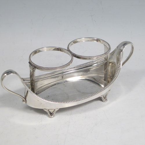 Antique Georgian sterling silver oil and vinegar set, having an oval boat-shaped body with applied bead-edged borders, two loop side handles, a pair of hand-cut crystal bottles with stoppers, and all sitting on four flange feet. Made by John Schofield of London in 1782. The dimensions of this fine hand-made silver oil and vinegar set are length 16.5 cms (6.5 inches), height (excl. bottles) 6.5 cms (2.5 inches), width 6.5 cms (2.5 inches), and the base weighs approx. 152g (5 troy ounces).