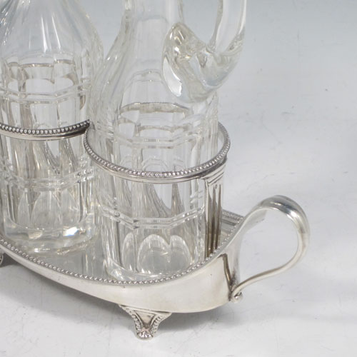 Antique Georgian sterling silver oil and vinegar set, having an oval boat-shaped body with applied bead-edged borders, two loop side handles, a pair of hand-cut crystal bottles with stoppers, and all sitting on four flange feet. Made by John Schofield of London in 1782. The dimensions of this fine hand-made silver oil and vinegar set are length 16.5 cms (6.5 inches), height (excl. bottles) 6.5 cms (2.5 inches), width 6.5 cms (2.5 inches), and the base weighs approx. 152g (5 troy ounces).