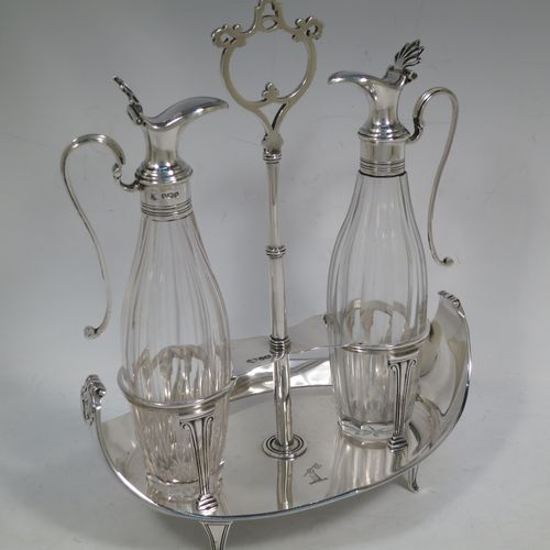 A very handosme Antique Sterling Silver oil and vinegar set in a neoclassical style, having an oval boat-shaped body with applied reed-edged borders, a two-bottle frame with hand-pierced handle, a pair of hand-cut round crystal bottles with panelled bodies and original hinged lid mounts with scroll handles, and all sitting on four flange feet. Made by Goldsmiths & Silversmiths of Sheffield in 1919. The dimensions of this fine hand-made antique silver oil and vinegar set are length 20 cms (8 inches), height 25.5 cms (10 inches), width 14 cms (5.5 inches), and it weighs approx. 250g (8 troy ounces).    