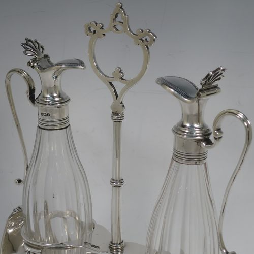 A very handosme Antique Sterling Silver oil and vinegar set in a neoclassical style, having an oval boat-shaped body with applied reed-edged borders, a two-bottle frame with hand-pierced handle, a pair of hand-cut round crystal bottles with panelled bodies and original hinged lid mounts with scroll handles, and all sitting on four flange feet. Made by Goldsmiths & Silversmiths of Sheffield in 1919. The dimensions of this fine hand-made antique silver oil and vinegar set are length 20 cms (8 inches), height 25.5 cms (10 inches), width 14 cms (5.5 inches), and it weighs approx. 250g (8 troy ounces).    