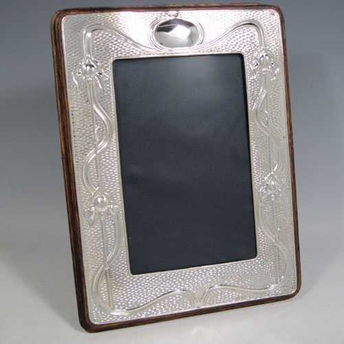 Antique Edwardian sterling silver Art Nouveau photograph frame, having a hand-made rectangular portrait body with rounded corners, a hand-chased border with lillies and reeds on a ripple patterned background, and an oval vacant cartouche, all pinned to a wood-backed easel frame. Made by A. & J. Zimmerman of Birmingham in 1903. The dimensions of this fine hand-made silver photo frame are height 18 cms (7 inches), and width 11 cms (4.3 inches).