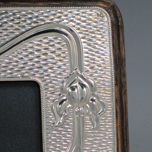 Antique Edwardian sterling silver Art Nouveau photograph frame, having a hand-made rectangular portrait body with rounded corners, a hand-chased border with lillies and reeds on a ripple patterned background, and an oval vacant cartouche, all pinned to a wood-backed easel frame. Made by A. & J. Zimmerman of Birmingham in 1903. The dimensions of this fine hand-made silver photo frame are height 18 cms (7 inches), and width 11 cms (4.3 inches).