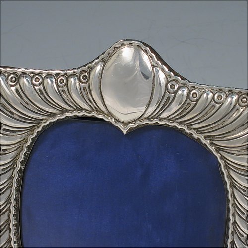 A very pretty Antique Victorian Sterling Silver photograph frame, having a heart-shaped aperture, surrounded by a hand-chased body with fluted decoration, and a wood-backed easel frame with brass fittings. Made by William Comyns of London in 1898. The internal dimensions of this fine hand-made antique silver photo frame are 12.5 cms (5 inches) high by 9.5 cms (3.75 inches) wide.   