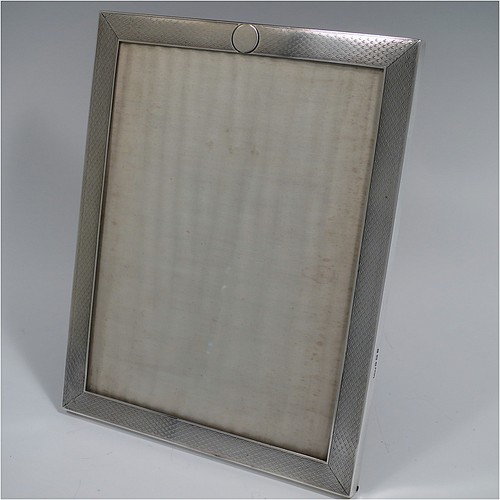 A Sterling Silver portrait photograph frame, having a hand-made rectangular body with machine-engraved and patterned border, a vacant round cartouche on the top border, and a brown wood-backed easel frame. Made by Percy James Finch of Birmingham in 1924. The dimensions of this fine hand-made silver photo frame are height 20 cms (8 inches), and width 15 cms (6 inches).    