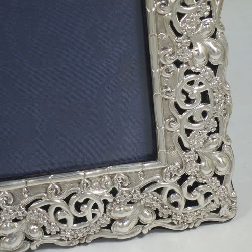 A large and very pretty Antique Edwardian Sterling Silver Art Nouveau style photograph frame, having a hand-chased body with flowers and scroll decoration, an inner bamboo style border, a top central vacant oval cartouche, and an original dark blue easel frame. Made by Simpson and Son of Birmingham in 1902. The internal dimensions of this fine hand-made antique silver photo frame are 27.5 cms (10.75 inches) high by 16.5 cms (6.5 inches) wide.    