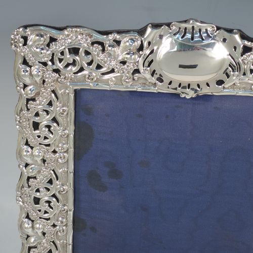 A large and very pretty Antique Edwardian Sterling Silver Art Nouveau style photograph frame, having a hand-chased body with flowers and scroll decoration, an inner bamboo style border, a top central vacant oval cartouche, and an original dark blue easel frame. Made by Simpson and Son of Birmingham in 1902. The internal dimensions of this fine hand-made antique silver photo frame are 27.5 cms (10.75 inches) high by 16.5 cms (6.5 inches) wide.    