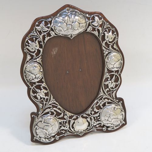 A very beautiful Art Nouveau Antique Victorian Sterling Silver photograph frame, having a heart-shaped aperture with a glass cover, surrounded by a hand-pierced border with floral and cherub decoration, and all pinned to an original wood-backed easel frame. This pretty antique silver photo frame was made by William Comyns of London in 1901. The internal dimensions of this fine hand-made Art Nouveau antique silver photo frame are height 11.5 cms (4.5 inches), and width 9 cms (3.5 inches).   