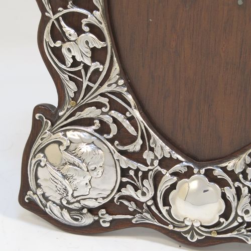 A very beautiful Art Nouveau Antique Victorian Sterling Silver photograph frame, having a heart-shaped aperture with a glass cover, surrounded by a hand-pierced border with floral and cherub decoration, and all pinned to an original wood-backed easel frame. This pretty antique silver photo frame was made by William Comyns of London in 1901. The internal dimensions of this fine hand-made Art Nouveau antique silver photo frame are height 11.5 cms (4.5 inches), and width 9 cms (3.5 inches).   