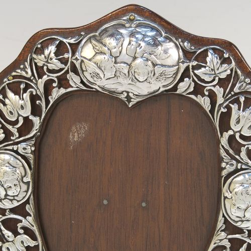 A very beautiful Art Nouveau Antique Victorian Sterling Silver photograph frame, having a heart-shaped aperture with a glass cover, surrounded by a hand-pierced border with floral and cherub decoration, and all pinned to an original wood-backed easel frame. This pretty antique silver photo frame was made by William Comyns of London in 1901. The internal dimensions of this fine hand-made Art Nouveau antique silver photo frame are height 11.5 cms (4.5 inches), and width 9 cms (3.5 inches).   