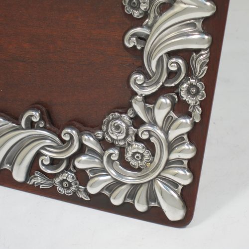 A very pretty Antique Victorian Sterling Silver photograph frame, having a rectangular landscape aperture, surrounded by a hand-pierced border with fluting, scroll-work, and floral decoration, and all pinned to a wood-backed easel frame. Made by William Comyns of London in 1895. The internal dimensions of this fine hand-made antique silver photo frame are 19 cms (7.5 inches) wide by 14 cms (5.5 inches) high.    