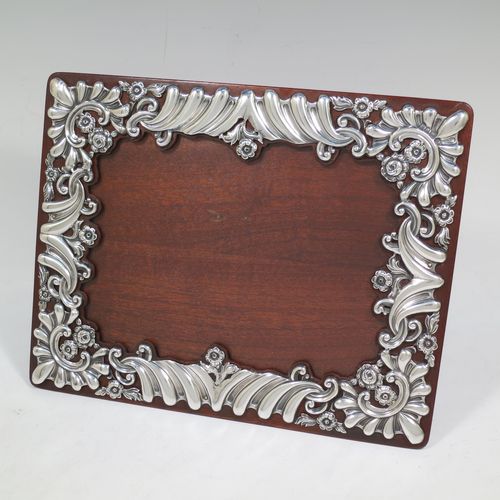 A very pretty Antique Victorian Sterling Silver photograph frame, having a rectangular landscape aperture, surrounded by a hand-pierced border with fluting, scroll-work, and floral decoration, and all pinned to a wood-backed easel frame. Made by William Comyns of London in 1895. The internal dimensions of this fine hand-made antique silver photo frame are 19 cms (7.5 inches) wide by 14 cms (5.5 inches) high.    