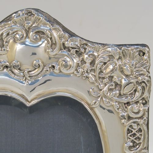 A very pretty Antique Edwardian Sterling Silver photograph frame, having a heart-shaped aperture, surrounded by a hand-chased body with floral and scroll decoration, and an original dark blue velvet-backed easel frame. This beautiful antique silver photo frame was made by James Deakin of Chester in 1902. The internal dimensions of this fine hand-made antique silver photo frame are 11.5 cms (4.5 inches) high by 9 cms (3.5 inches) wide. Please note that the velvet backing is slightly worn and faded.   