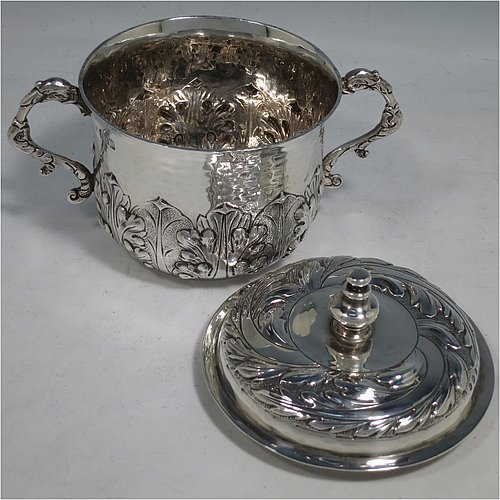 An Antique Edwardian Britannia Standard Silver porringer, having a round baluster body with a hand-hammered finish and hand-chased anthemion and floral decoration, a lift-off lid with matching floral work and a cast round finial, and two cast floral handles. Made by George Fox of London in 1906. The dimensions of this fine hand-made antique Britannia silver porringer and lid are height 11.5 cms (4.5 inches), spread across arms 16 cms (6.3 inches), and it weighs approx. 370g (12 troy ounces).    