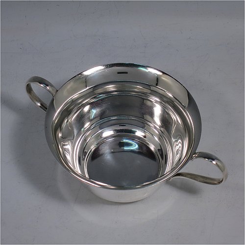 A Sterling Silver very simple porringer, having a plain round body, with two scroll side handles, and all sitting on a flat base. Made by William Hutton & Sons of Sheffield in 1918. The dimensions of this fine hand-made silver porringer are height 6 cms (2.3 inches), spread across arms 16 cms (6.3 inches), and it weighs approx. 140g (4.5 troy ounces).   