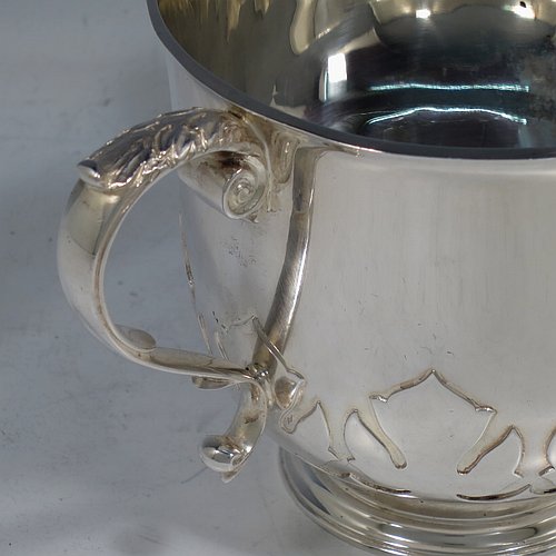 A heavy Sterling Silver three-handled porringer or loving cup, having a round body with tucked under belly and applied cut-card work, three cast scroll side-handles, and sitting on a pedestal foot. Made by Goldsmiths & Silversmiths of London in 1937. The dimensions of this fine hand-made silver loving cup or porringer are height 9.5 cms (3.75 inches), diameter 10 cms (4 inches), and it weighs approx. 417g (13.5 troy ounces).   