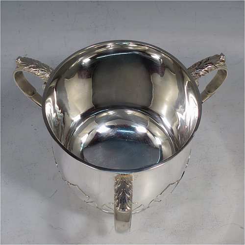 A heavy Sterling Silver three-handled porringer or loving cup, having a round body with tucked under belly and applied cut-card work, three cast scroll side-handles, and sitting on a pedestal foot. Made by Goldsmiths & Silversmiths of London in 1937. The dimensions of this fine hand-made silver loving cup or porringer are height 9.5 cms (3.75 inches), diameter 10 cms (4 inches), and it weighs approx. 417g (13.5 troy ounces).   