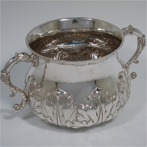 A heavy Sterling Silver porringer, having a round bellied body with a slight hand-hammered finish and hand-chased anthemion and floral decoration, and two cast side-handles with stylised dolphin heads. Made by Robert Comyns of London in 1931. The dimensions of this fine hand-made silver porringer are height 7 cms (2.75 inches), spread across arms 14 cms (5.5 inches), and it weighs approx. 247g (8 troy ounces).    