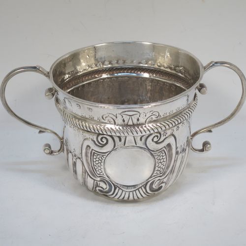 A very handsome Antique Queen Anne Britannia Standard Silver porringer, having a round bellied body with hand-chased fluted and scroll decoration, with a round cartouche on one side, two scroll side-handles, and sitting on a flat base. Made by Seth Lofthouse (Prob.) of London in 1709. The dimensions of this fine hand-made antique Britannia silver porringer are height 8 cms (3 inches), spread across handles 16 cms (6.25 inches), and it weighs approx. 156g (5 troy ounces).  