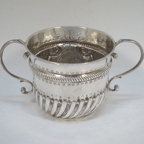 A very handsome Antique Queen Anne Britannia Standard Silver porringer, having a round bellied body with hand-chased fluted and scroll decoration, with a round cartouche on one side, two scroll side-handles, and sitting on a flat base. Made by Seth Lofthouse (Prob.) of London in 1709. The dimensions of this fine hand-made antique Britannia silver porringer are height 8 cms (3 inches), spread across handles 16 cms (6.25 inches), and it weighs approx. 156g (5 troy ounces).  