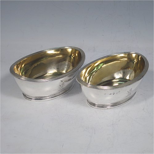 An Antique Georgian Sterling Silver pair of salt cellars, in an oval bath-shaped style, having plain oval bodies, with gold-gilt interiors, applied reeded borders, all sitting on reeded collet feet. Made by either Henry Nutting OR Hannah Northcote of London in 1804. The dimensions of these fine hand-made antique silver salt cellars are length 9.5 cms (3.75 inches), width 6.5 cms (2.5 inches), height 4 cms (1.5 inches), and they weigh a total of approx. 185g (6 troy ounces). Please note that both salt cellars are part-crested.