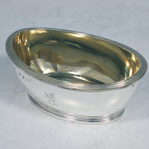 An Antique Georgian Sterling Silver pair of salt cellars, in an oval bath-shaped style, having plain oval bodies, with gold-gilt interiors, applied reeded borders, all sitting on reeded collet feet. Made by either Henry Nutting OR Hannah Northcote of London in 1804. The dimensions of these fine hand-made antique silver salt cellars are length 9.5 cms (3.75 inches), width 6.5 cms (2.5 inches), height 4 cms (1.5 inches), and they weigh a total of approx. 185g (6 troy ounces). Please note that both salt cellars are part-crested.