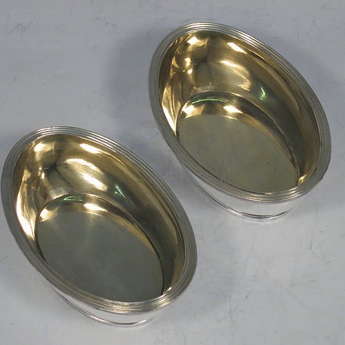 An Antique Georgian Sterling Silver pair of salt cellars, in an oval bath-shaped style, having plain oval bodies, with gold-gilt interiors, applied reeded borders, all sitting on reeded collet feet. Made by either Henry Nutting OR Hannah Northcote of London in 1804. The dimensions of these fine hand-made antique silver salt cellars are length 9.5 cms (3.75 inches), width 6.5 cms (2.5 inches), height 4 cms (1.5 inches), and they weigh a total of approx. 185g (6 troy ounces). Please note that both salt cellars are part-crested.