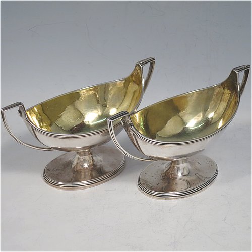 An Antique Georgian Sterling Silver pair of salt cellars, in a boat-shaped style, having plain oval bodies, with gold-gilt interiors, applied reeded borders, and reeded side-handles, all sitting on pedestal feet. Made by either Henry Nutting OR Hannah Northcote of London in 1803. The dimensions of these fine hand-made antique silver salt cellars are length 14 cms (5.5 inches), width 6 cms (2.3 inches), height 7.5 cms (3 inches), and they weigh a total of approx. 217g (7 troy ounces).    