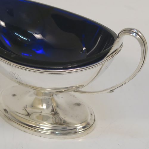 A very handsome Antique Georgian Sterling Silver pair of salt cellars, in a boat-shaped neoclassical style, having plain oval bodies, with blue-glass liners, applied reeded borders, and reeded side-handles, all sitting on pedestal feet. These elegant antique silver salt cellars were made by William Frisbee of London in 1792. The dimensions of these fine hand-made antique silver salt cellars are length 13.5 cms (5.3 inches), width 6 cms (2.3 inches), height 8 cms (3.25 inches), and they weigh a total of approx. 180g (5.8 troy ounces). Please note that both salt cellars have engraved crests.   