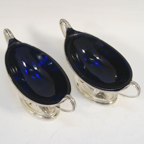 A very handsome Antique Georgian Sterling Silver pair of salt cellars, in a boat-shaped neoclassical style, having plain oval bodies, with blue-glass liners, applied reeded borders, and reeded side-handles, all sitting on pedestal feet. These elegant antique silver salt cellars were made by William Frisbee of London in 1792. The dimensions of these fine hand-made antique silver salt cellars are length 13.5 cms (5.3 inches), width 6 cms (2.3 inches), height 8 cms (3.25 inches), and they weigh a total of approx. 180g (5.8 troy ounces). Please note that both salt cellars have engraved crests.   