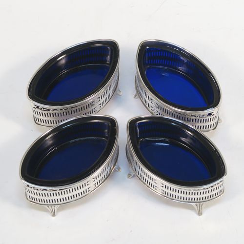 An elegant set of four Antique Edwardian Sterling Silver salt cellars in a Neoclassical style, having oval boat-shaped bodies with hand-pierced galleried sides, internal blue glass liners, and sitting on four fluted flange feet. These beautiful antique silver salt cellars were made by Jackson and Fullerton of London in 1909. The dimensions of this fine hand-made set of four silver salt cellars are length 9 cms (3.5 inches), height 5 cms (2 inches), width 5 cms (2 inches), and they weigh a total of approx. 214g (6.9 troy ounces).   