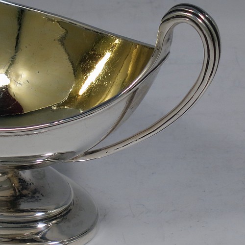 An Antique Georgian Sterling Silver pair of salt cellars, in a boat-shaped neoclassical style, having plain oval bodies, with gold-gilt interiors, applied reeded borders, and reeded side-handles, all sitting on pedestal feet. Made by John Wakelin and William Taylor of London in 1785 (having the rare Incuse duty mark). The dimensions of these fine hand-made antique silver salt cellars are length 13.5 cms (5.3 inches), width 6.5 cms (2.5 inches), height 8 cms (3.25 inches), and they weigh a total of approx. 214g (6.9 troy ounces). Please note that both salt cellars have engraved crests.