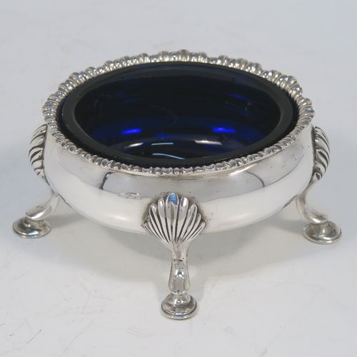 A very handsome matched pair of Antique Georgian and Victorian Sterling Silver salt cellars, having plain oval bodies, with blue-glass liners, applied shaped gadroon borders, and all sitting on four cast hoof feet with shell shoulders. These elegant silver salt cellars were made by Robert Hennell of London in 1819 and 1875. The dimensions of these fine hand-made antique silver salt cellars are length 9 cms (3.5 inches), width 8 cms (3 inches), height 4.5 cms (1.75 inches), and they weigh a total of approx. 170g (5.5 troy ounces).  