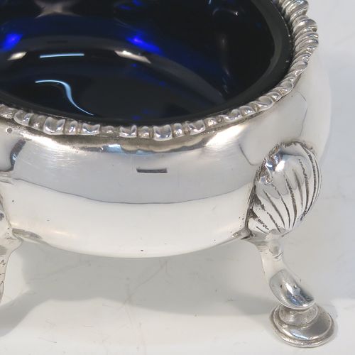 A very handsome matched pair of Antique Georgian and Victorian Sterling Silver salt cellars, having plain oval bodies, with blue-glass liners, applied shaped gadroon borders, and all sitting on four cast hoof feet with shell shoulders. These elegant silver salt cellars were made by Robert Hennell of London in 1819 and 1875. The dimensions of these fine hand-made antique silver salt cellars are length 9 cms (3.5 inches), width 8 cms (3 inches), height 4.5 cms (1.75 inches), and they weigh a total of approx. 170g (5.5 troy ounces).  