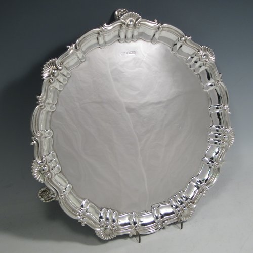 A Sterling silver salver, having a round body, with a plain burnished ground, an applied Shell & Scroll  border, and sitting on three shell feet. Made by Walker and Hall of Sheffield in 1919. The dimensions of this fine hand-made silver salver are diameter 31 cms (12 inches), and it weighs approx. 658g (21 troy ounces).    