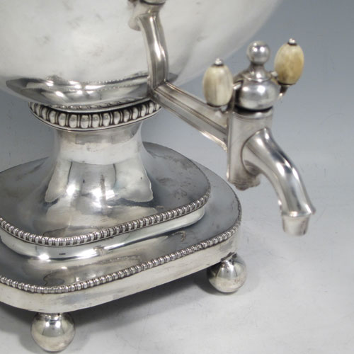 Antique Georgian Old Sheffield plated urn-style samovar having a plain rectangular body with rounded corners and tapering sides, a lift-off lid with finial, with original liner for heating, two side handles, a spigot with ivory handles, with applied gadroon-edge borders, and all sitting on a pedestal foot with four ball feet. Made in ca. 1810. The dimensions of this fine hand-made Old Sheffield plated silver samovar are height 33 cms (13 inches), width 28 cms (11 inches), and depth incl. spigot 23 cms (9 inches).