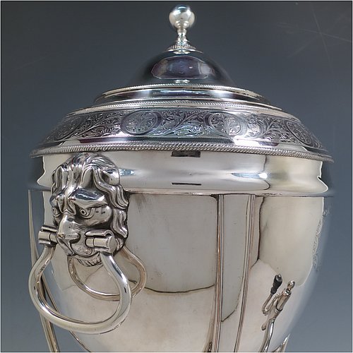 An Antique Georgian Old Sheffield plated urn-style samovar having a plain round body with applied gadroon borders, a band of hand-engraved floral decoration, and cast lion-mask handles. Having a lift-off lid with ball finial, a spigot with wooden finial, and all sitting on four lions-paw feet with a base that includes a removable burner and four ball feet. Made in ca. 1800. The dimensions of this fine hand-made Old Sheffield silver plated samovar are height 48 cms (19 inches), width 26 cms (10 inches), and depth incl. spigot 28 cms (11 inches).   