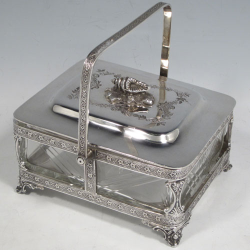 Antique Victorian silver plated sardine dish, having a rectangular body with rounded corners, a cut-crystal liner sitting in a frame which has chased ivy-work, a lift-off lid with cast conch shell finial, a floral swing handle, and all sitting on four cast foliate feet. Made by Walker and Hall of Sheffield in ca. 1880. The dimenions of this fine hand-made silver-plated sardine dish are length 14 cms (5.5 inches), width 12 cms (4.75 inches), and height (excluding handles) 8 cms (3 inches).