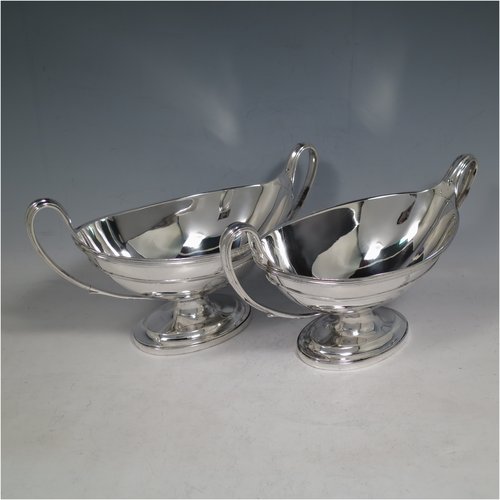 An Antique Georgian Sterling Silver pair of heavy sauce tureens, having oval neoclassical boat-shaped bodies with applied reeded borders, with cast reeded loop handles, and all sitting on cast oval pedestal feet. Made by Cornelius Bland y of London in 1792. The dimensions of this fine hand-made antique silver pair of sauce tureens are height 14 cms (5.5 inches), length 24.5 cms (9.75 inches), width 11 cms (4.25 inches), with a total weight of approx. 960g (31 troy ounces). Please note that both theses items are crested.  