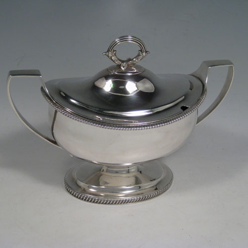    Antique Georgian George III sauce tureen, having an oval plain body, gadroon borders, lift off lid with asparagus loop handle and slot for sauce ladle, two side handles, and sitting on a pedestal foot. Made by Robert and Samuel Hennell of London in 1805. Length 21.5 cms (8.5 inches), width 11 cms (4.3 inches), height 18 cms (6.3 inches). Total weight approx. 545g (17.6 troy ounces).