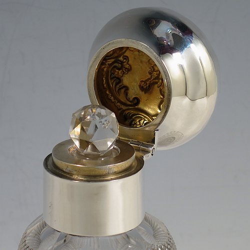 An Antique Victorian Sterling Silver and hand-cut crystal large table scent bottle, having a hand-chased round hinged lid with floral and figural decoration, a plain round mount, an internal stopper, and an unusual shaped hand-cut crystal body with floral, swags, bows, and fluted decoration. Made by William Comyns of London in 1900. The dimensions of this fine hand-made antique silver & crystal scent bottle are height 18 cms (7 inches), and diameter 10 cms (4 inches).    