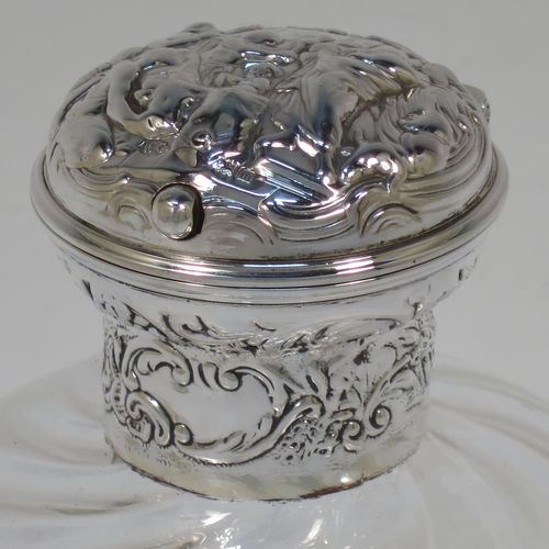 A very pretty and unusual pair of Antique Edwardian Sterling Silver and hand-cut crystal table scent bottles, having round mounts with hinged lids and internal stoppers, the lids with hand-chased figural scene decoration and push-button snap fits. The crystal bodies with rounded square cross-sections and swirl fluted decoration, and all sitting on flat bases. Made by William Comyns of London in 1907. The dimensions of these fine hand-made antique silver and crystal scent bottles are height 12.5 cms (5 inches), and 8.5cms (3.3 inches) square.  