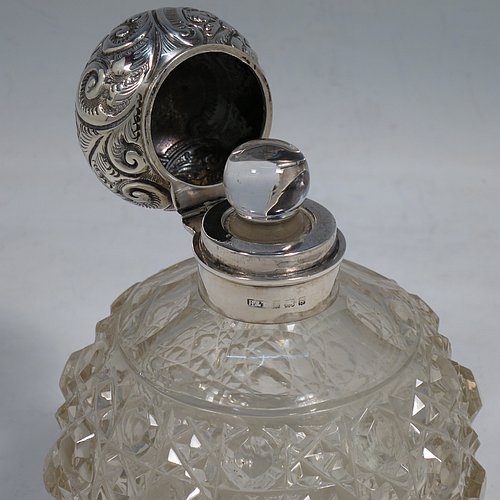 An Antique Edwardian Sterling Silver and hand-cut crystal table scent bottle, having a hand-chased round mount with floral decoration, a hinged lid, an internal stopper, and hand-cut crystal main body in the Hobnail pattern. Made by Hilliard & Thomason of Birmingham in 1906. The dimensions of this fine hand-made antique silver and crystal scent bottle are height 13 cms (5 inches), and diameter 9 cms (3.5 inches).    