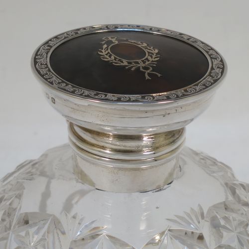 A very pretty Sterling Silver and inlaid tortoise-shell hand-cut crystal table scent bottle, having a plain round mount, a hinged lid with an inlaid  tortoise-shell cover, an internal stopper, and hand-cut main body with reeding and star-cut decoration. Made by Henry Miller of Birmingham in 1923. The dimensions of this fine hand-made silver and tortoise shell scent bottle are height 12.5 cms (5 inches), and diameter 9.5 cms (3.75 inches).  