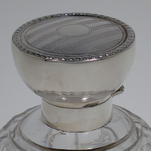 An Antique Sterling Silver and hand-cut crystal large table scent bottle, having a plain round mount, a hinged lid with an applied floral border and bands of engine-turned engraved decoration, an internal stopper, and a hand-cut crystal round main body with geometrical decoration. Made by Synyer and Beddoes of Birmingham in 1915. The dimensions of this fine hand-made antique silver and crystal scent bottle are height 11.5 cms (4.5 inches), and diameter 8 cms (3.25 inches).    