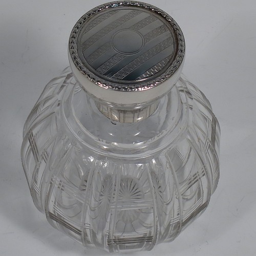 An Antique Sterling Silver and hand-cut crystal large table scent bottle, having a plain round mount, a hinged lid with an applied floral border and bands of engine-turned engraved decoration, an internal stopper, and a hand-cut crystal round main body with geometrical decoration. Made by Synyer and Beddoes of Birmingham in 1915. The dimensions of this fine hand-made antique silver and crystal scent bottle are height 11.5 cms (4.5 inches), and diameter 8 cms (3.25 inches).    